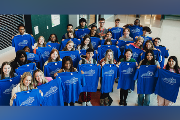 A large group of high school students standing in the school lobby. The students are holding up t shirts from the UK College of Education.