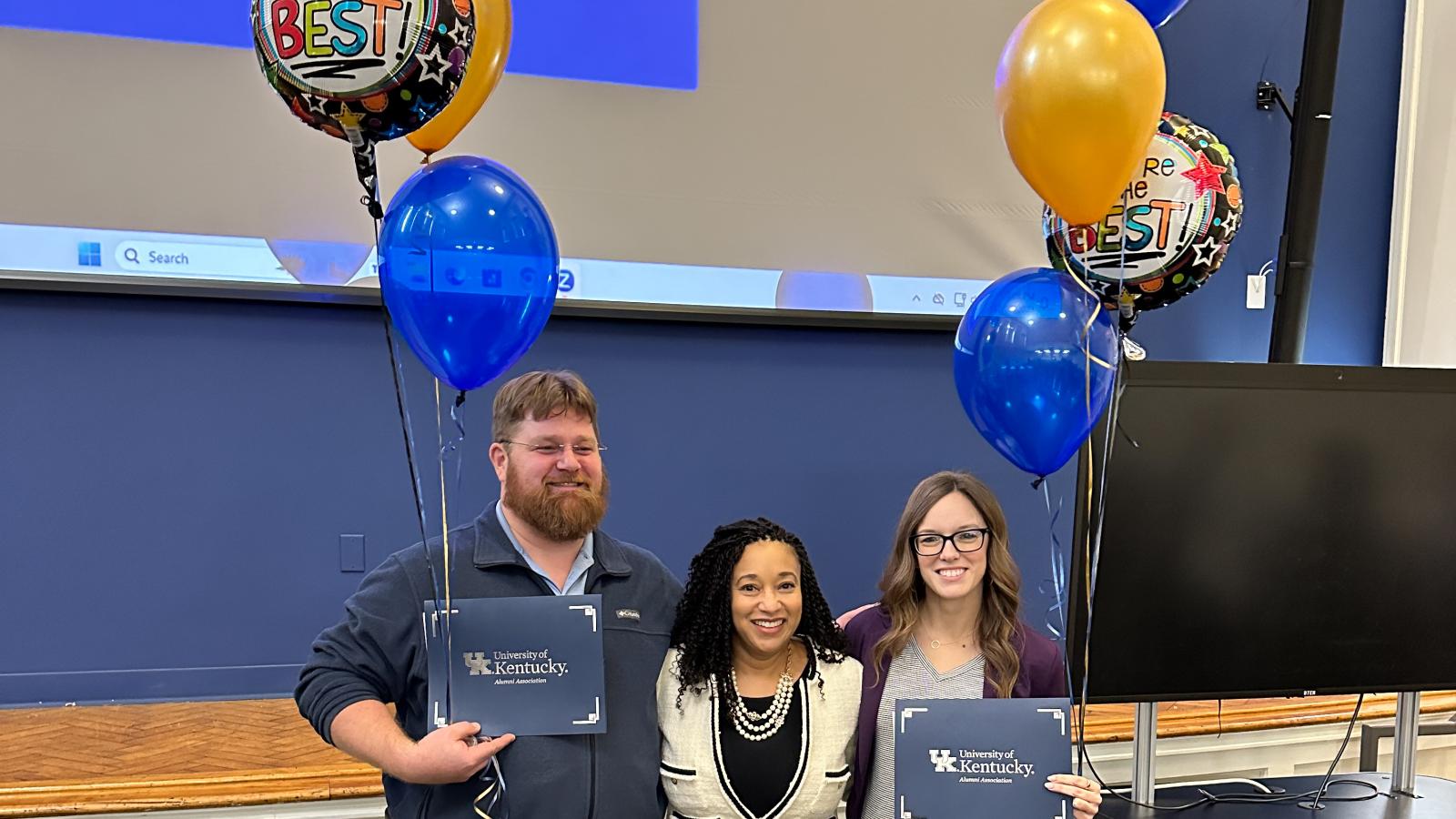 Three individuals holding awards and balloons.