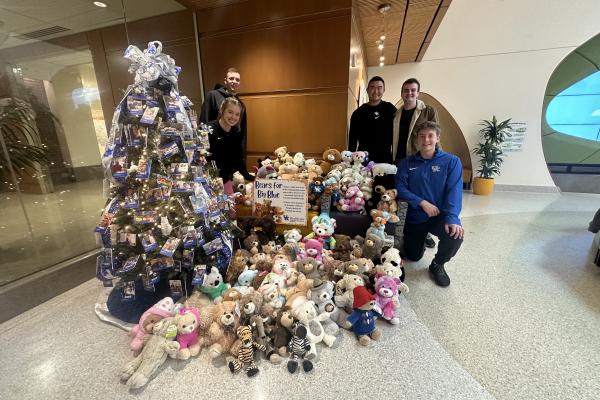 Five students standing next to a Christmas tree and stuffed animal donations for the children's hospital