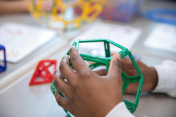 A child's hands holding a green circular ball designed for hands-on learning.