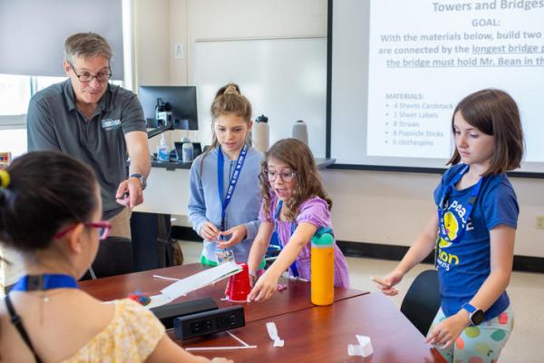 A professor stands with a group of children conducting an experiment on a table