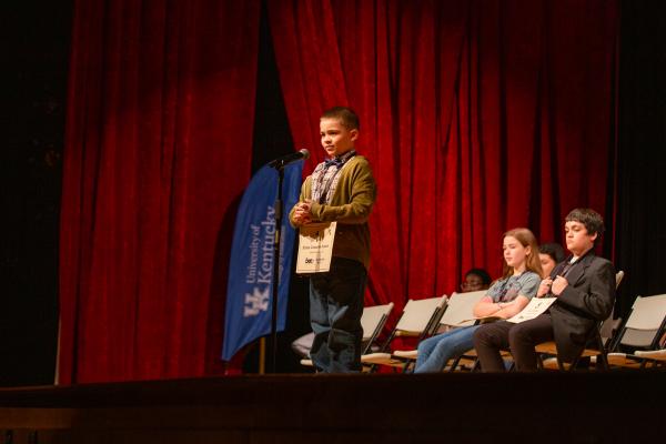 Boy stands behind microphone to spell a word in a 2024 spelling bee