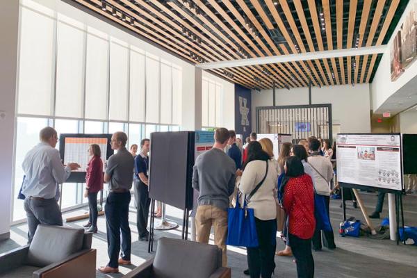 a group of people look at various research posters at a conference