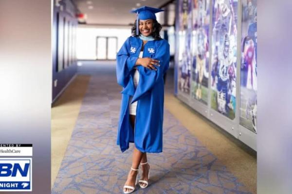 Jocelyn Grimsley wearing a graduation gown standing near a football mural