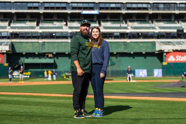 Man and woman stand on grass of a baseball field