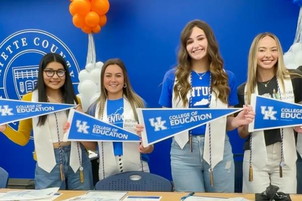 Four high school students stand holding UK College of Education pennants