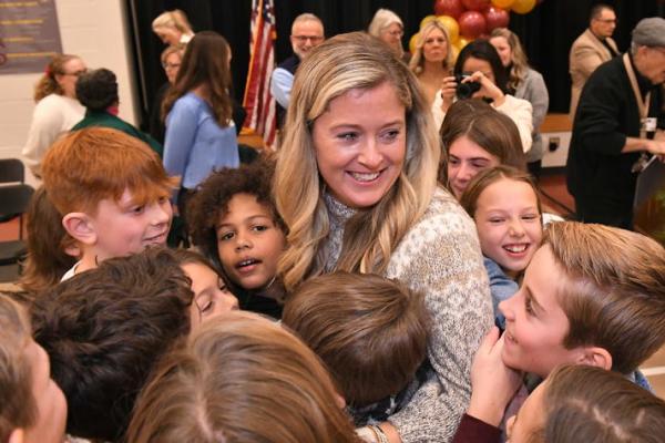 A teacher is surrounded by students who are hugging her