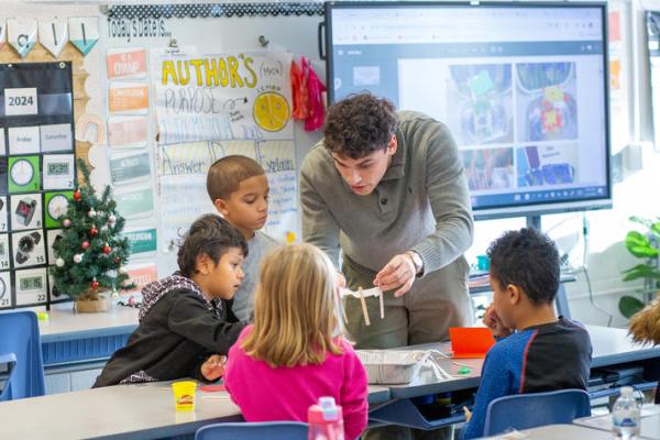 A UK student stands with a group of four elementary students to demonstrate a lesson