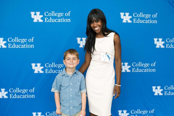 Young boy stands next to woman against UK College of Education backdrop