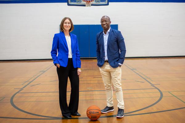 A woman and a man stand on a basketball court with a basketball near their feet