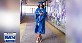 Jocelyn Grimsley wearing a graduation gown standing near a football mural
