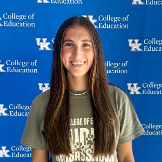 Student standing in front of blue UK College of Education backdrop