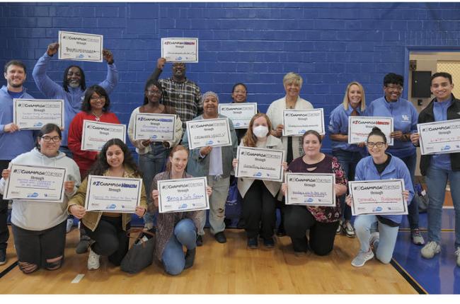 Group of participants in I Champion Health holding signs saying how they champion health in a gymnasium