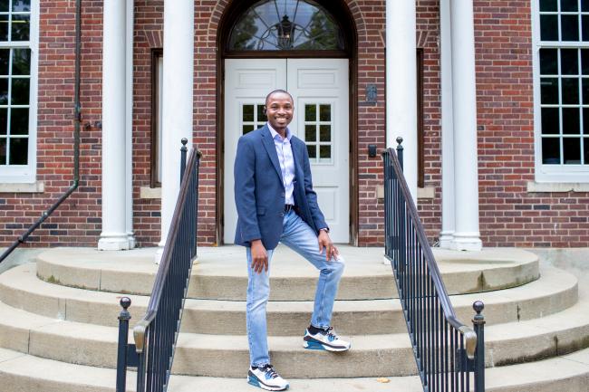 Man wearing a sport jacket, jeans, and tennis shoes standing on front steps of Taylor Education Building