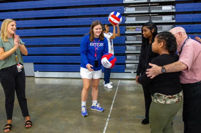 Teacher stands at center of photo holding a volleyball while two additional teachers and a student look on