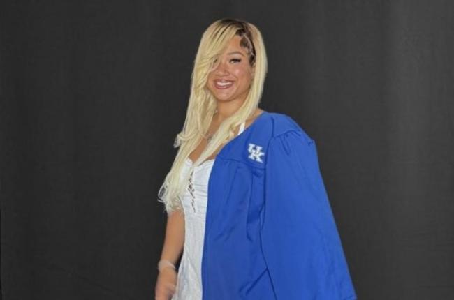 Photo of smiling woman wearing a blue graduation gown draped over one shoulder.