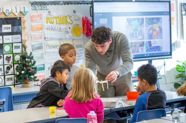 A UK student stands with a group of four elementary students to demonstrate a lesson