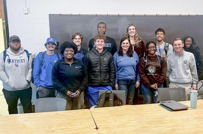 A group of students pose for a photo in front of a chalkboard in a classroom