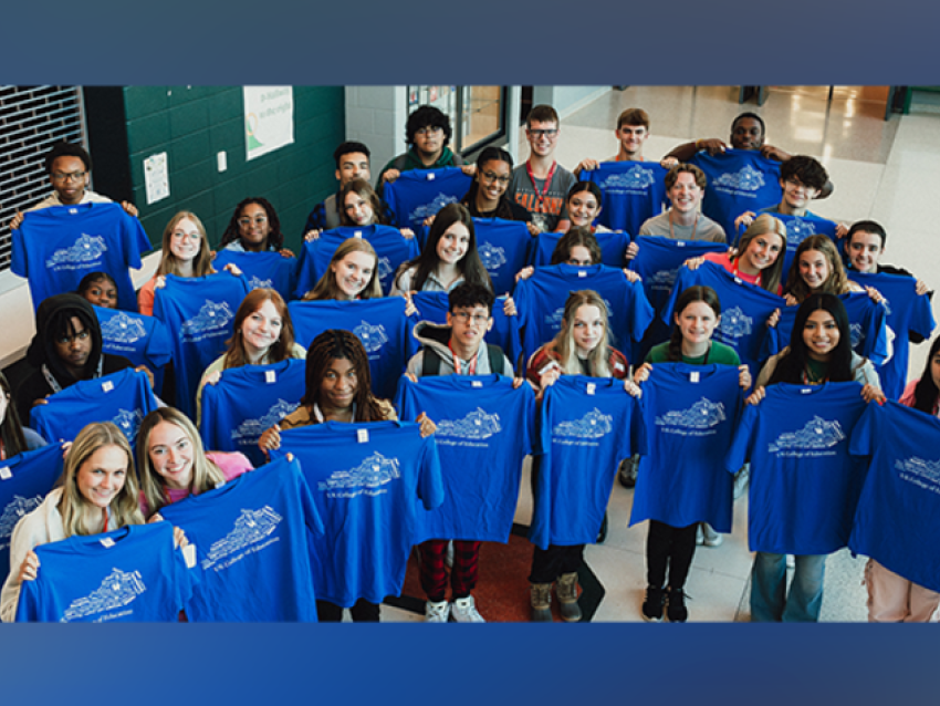 A large group of high school students standing in the school lobby. The students are holding up t shirts from the UK College of Education.