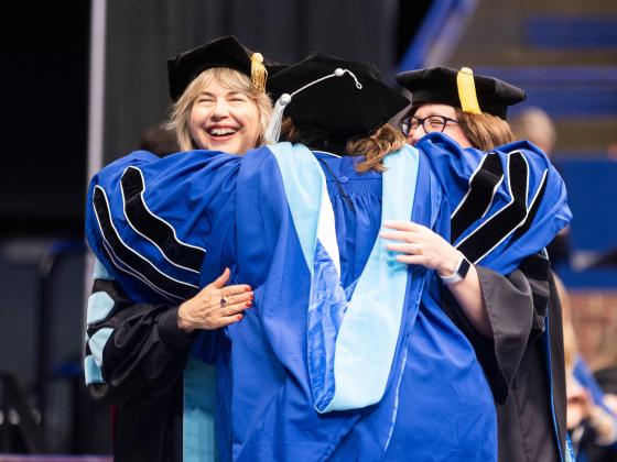Doctoral graduate hugging faculty members